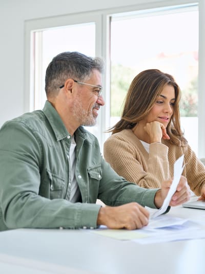 happy middle aged couple deciding on RV rental vs buying by sitting in front of laptop and going though finances